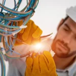 Licensed electrician in a hard hat and safety gloves working on electrical wiring