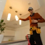 Electrician on a step ladder adjusting a pendant light fixture in a residential kitchen