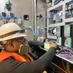 Technician working inside an industrial electrical control cabinet containing variable-frequency drives and terminal blocks
